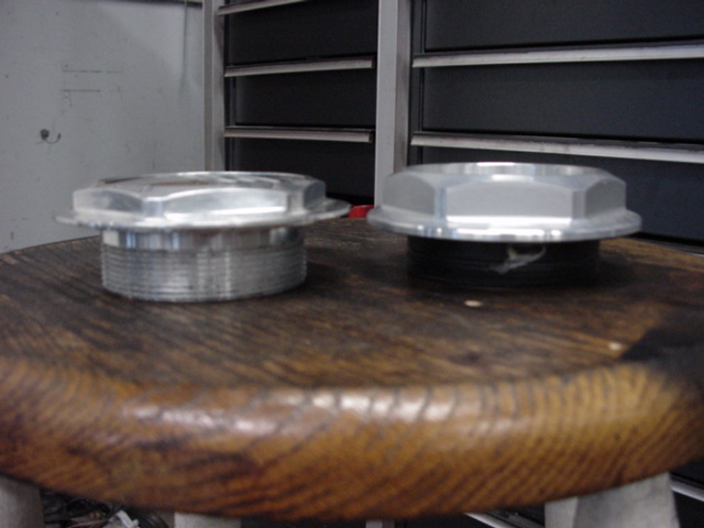 Two silver metal caps with hexagonal tops sit on a wooden surface in front of a metal cabinet