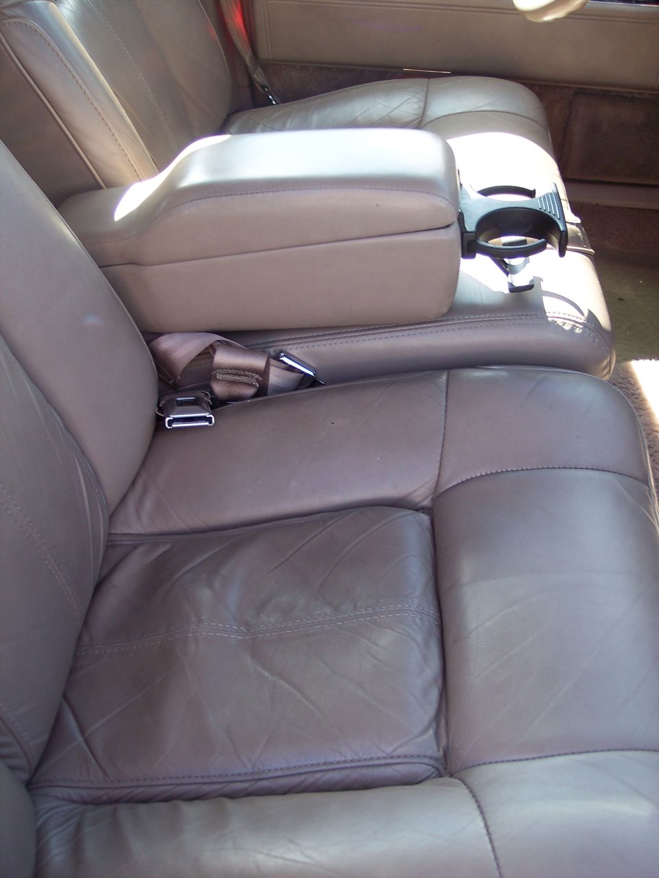 Tan leather front seats with fold-down armrest and black cup holder in a car interior