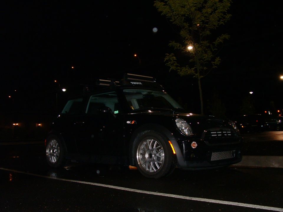 Black Mini Cooper with a Thule roof rack parked at night