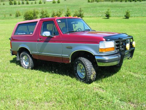 1995 Ford Bronco - A two-tone red and silver 1995 Ford Bronco is shown from the front-three-quarter view in a grassy field.