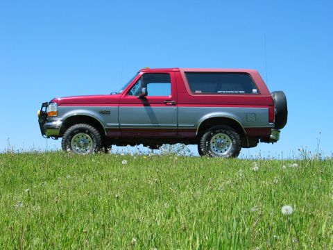 1995 Ford Bronco - Side view of a two-tone red and silver 1995 Ford Bronco on a grassy hill with a clear blue sky.
