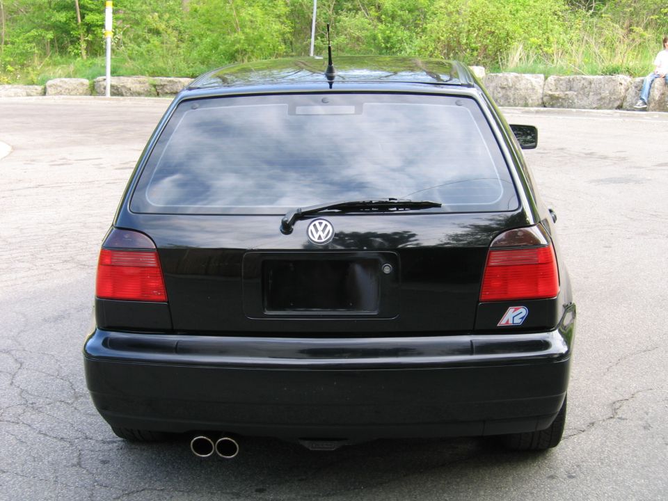 Black hatchback rear view with dual exhaust pipes and a Volkswagen logo