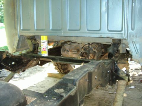 1985 Ford Bronco - The underside of a truck is visible, with a spray can of lubricant resting on the frame.