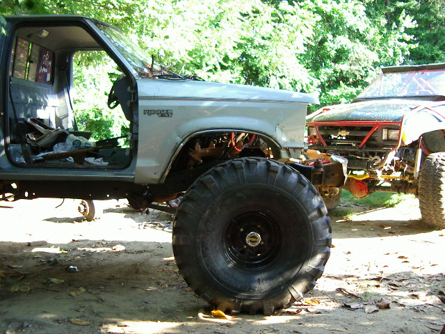Ford Ranger pickup truck with large tires, missing doors and hood. Another off-road vehicle is parked next to it
