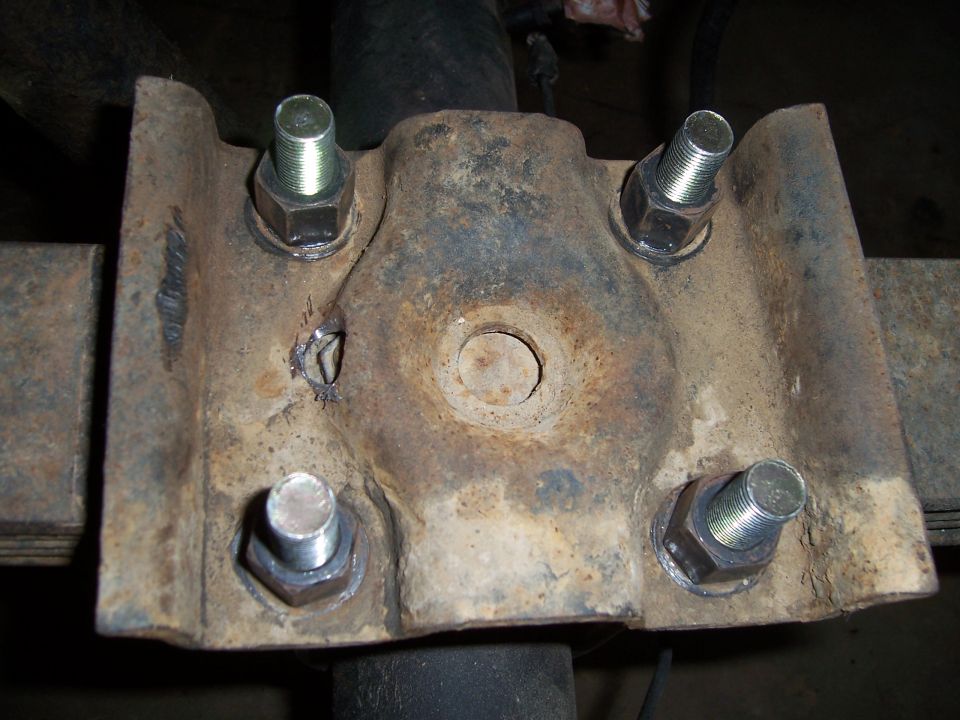 Underside of a leaf-spring U-bolt plate showing heavy surface rust and a welded crack repair
