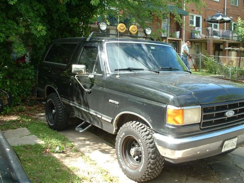 1989 Ford Bronco - A dark-colored 1989 Ford Bronco is parked outdoors, roof-mounted lights and off-road tires.