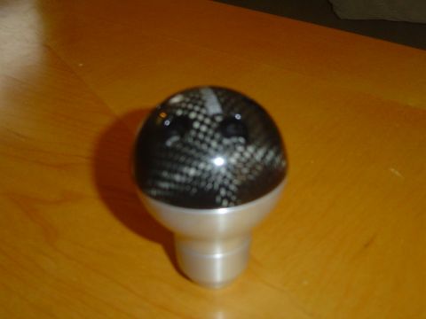 1996 Ford Probe - A carbon fiber shift knob with a silver base is shown on a wooden surface.