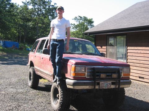 1991 Ford Explorer - A red 1991 Ford Explorer is shown lifted with off-road tires, a man standing on its hood. The license plate reads XEE 875.