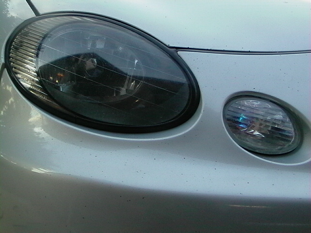 Silver car front bumper with dark-tinted headlight and smaller fog light