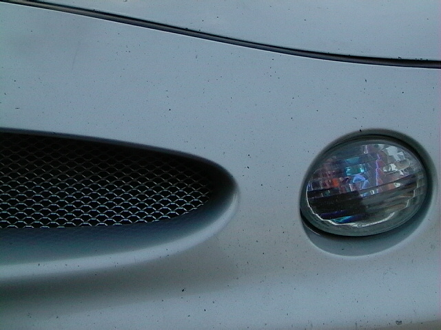 Close-up of a car's front end, showing a headlight and part of the grille