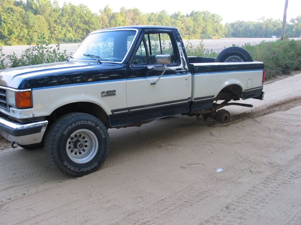 Two-tone cream and dark blue pickup truck with a missing rear wheel, spare tire in bed