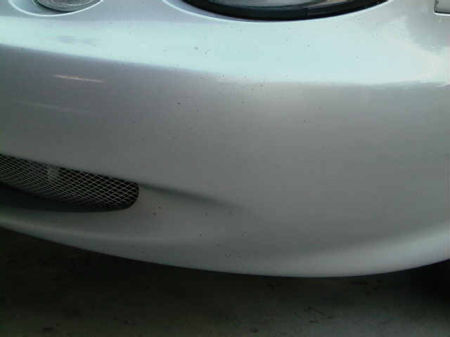 Close-up of a car's front bumper with a mesh grille and part of a headlight visible