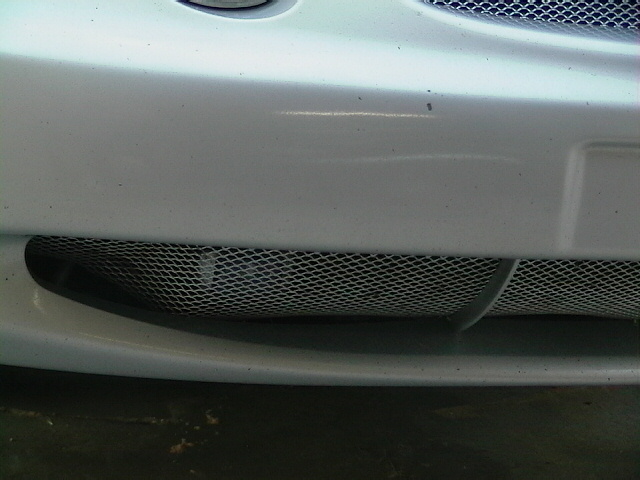 Close-up of a car's front bumper with a mesh grille and a Supermotors.net watermark