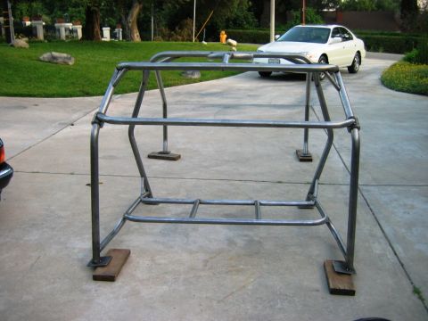 1985 Ford Bronco - A custom metal roll cage is shown assembled on a concrete driveway, with a white sedan in the background.
