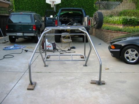 1985 Ford Bronco - A custom roll cage is being worked on in a driveway, with two SUVs parked nearby.