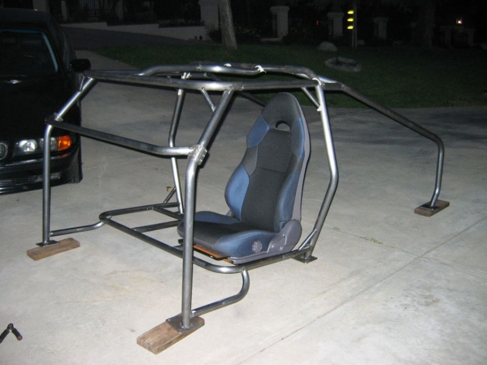 Bare metal roll cage frame with single racing seat on a driveway at night
