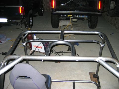 1985 Ford Bronco - A custom roll cage is being fabricated inside a vehicle, with a Hobart welder visible in the background and two trucks parked behind.