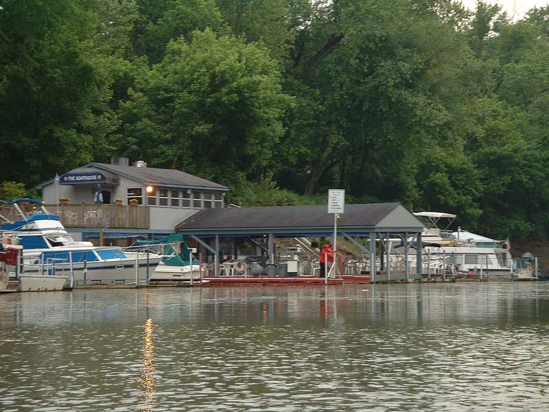 Boats docked at a marina with a boathouse and trees in the background