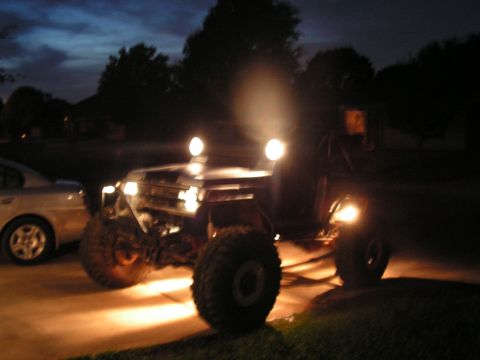 1978 Ford Bronco - An off-road SUV with its headlights on is parked next to a sedan in the twilight.