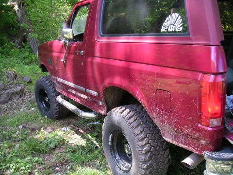 1994 Ford Bronco - Side view of a red 1994 Ford Bronco, modified for off-road use, parked outdoors.