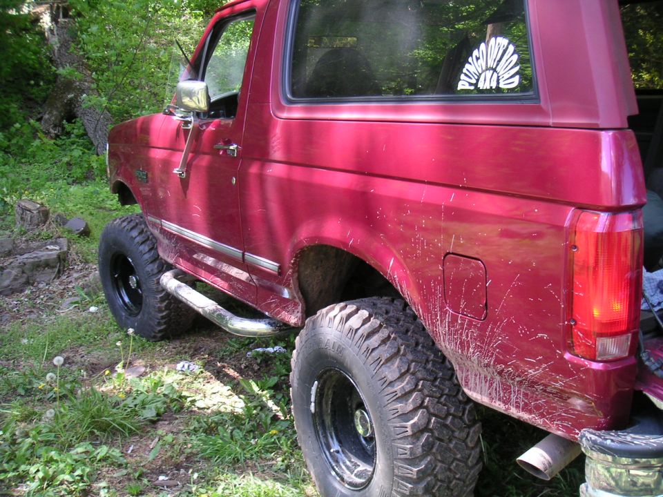 Red 1994 Ford Bronco with lifted suspension and mud tires parked on grassy terrain