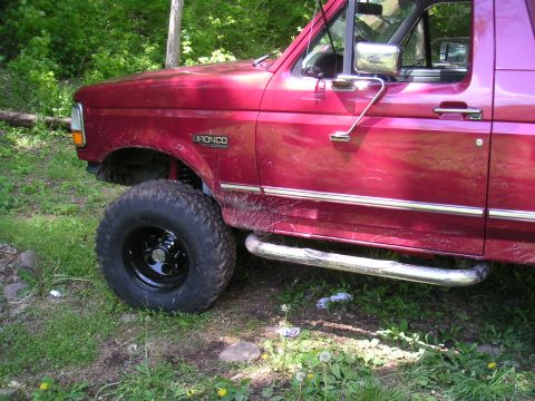 1994 Ford Bronco - A red Ford Bronco is parked off-road, showing its side profile and off-road tires.