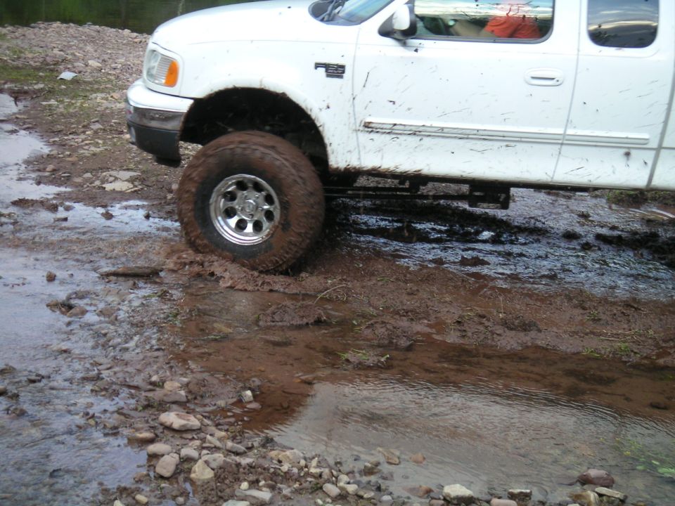 White pickup truck with lifted suspension stuck in a muddy stream