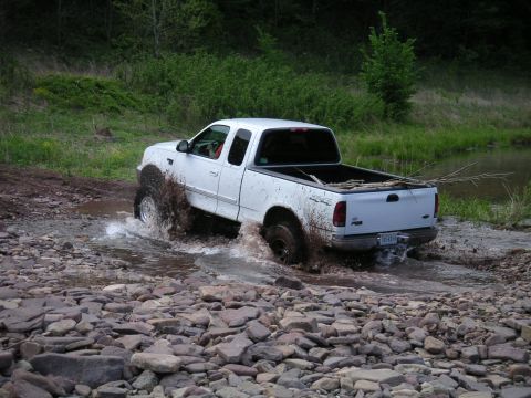 1994 Ford Bronco - White 1997 Ford F-150 navigates a rocky stream during an outdoor excursion.