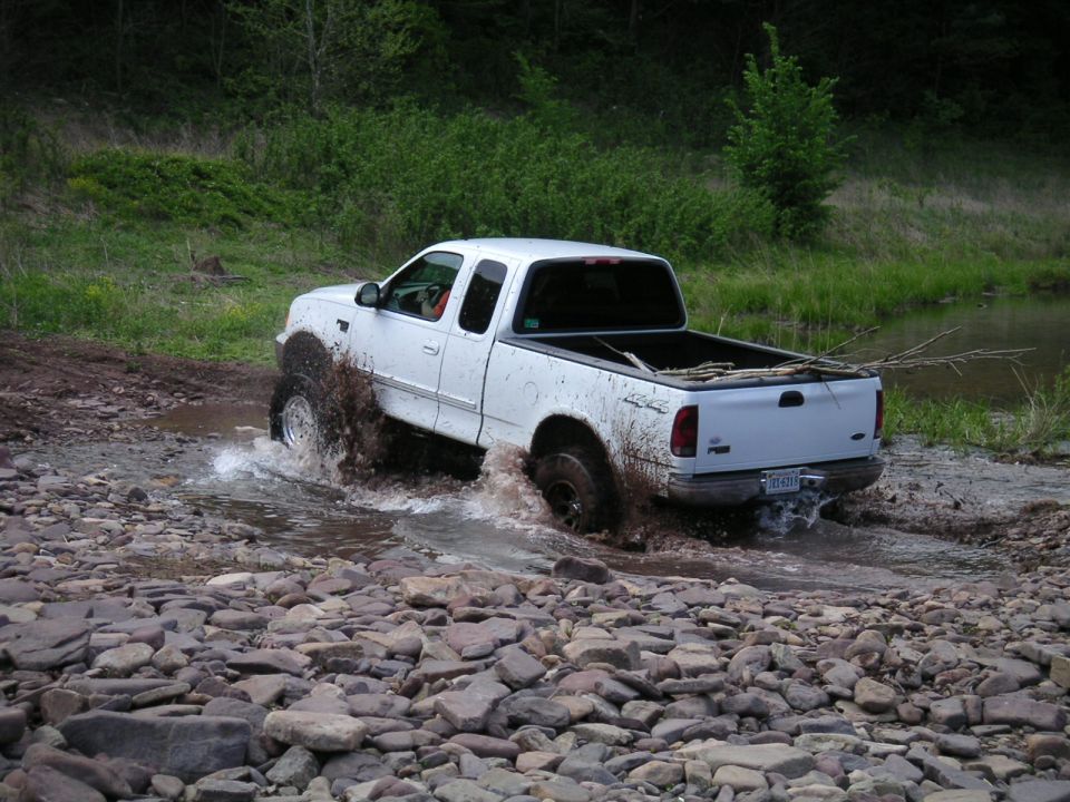 White 1997 Ford F-150 driving through water and rocks
