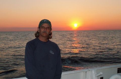 1988 Ford Bronco - A man poses for a photo on a boat as the sun sets over the water.
