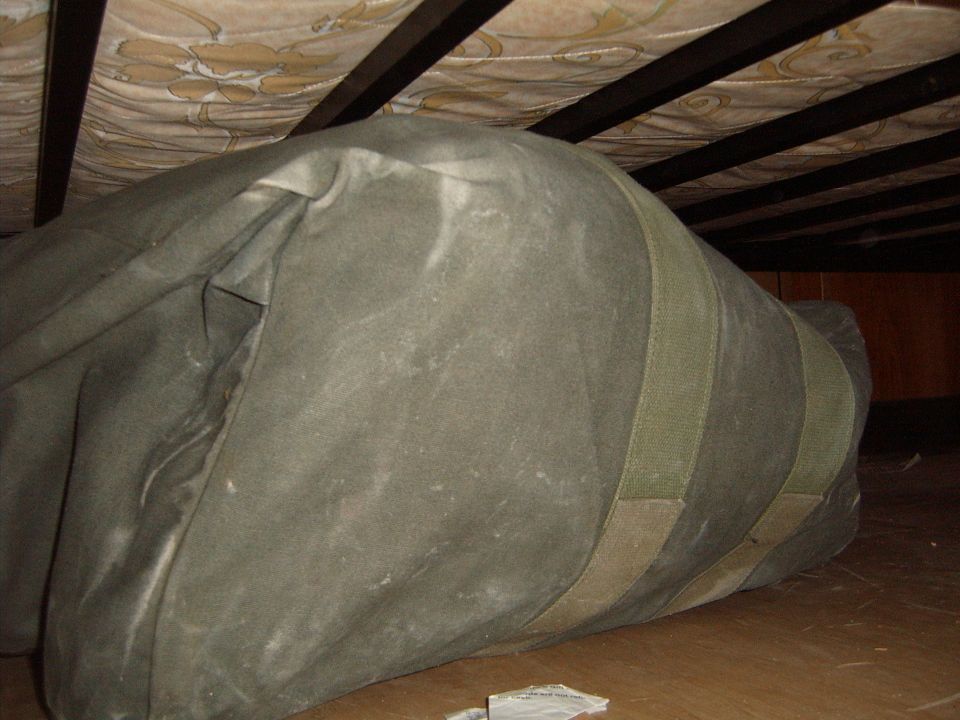Large green duffel bag stored under a bed frame with wooden slats