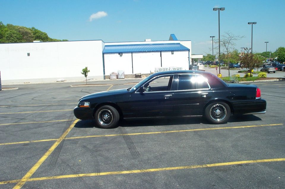 Black Ford Crown Victoria sedan in side profile in an empty parking lot