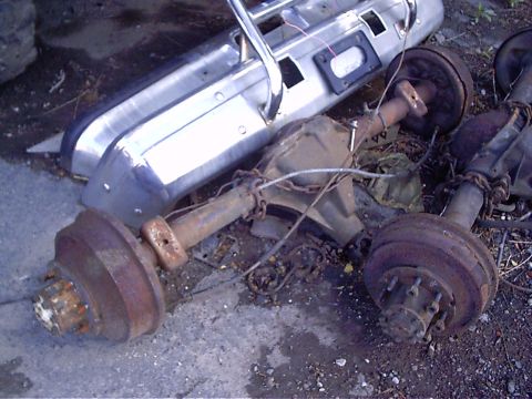 1979 Ford Bronco - Spare parts including bumpers and rear axles are piled on the ground.