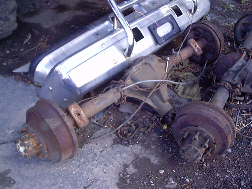 Two chrome bumpers and two rusty rear axles with brake drums