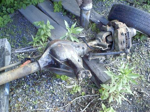 1979 Ford Bronco - A rusty vehicle rear axle assembly sits outdoors on wooden planks and gravel.