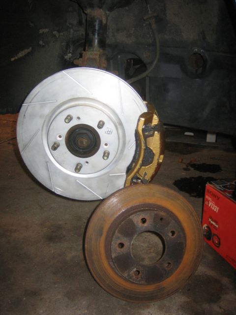 1995 Ford Probe - A new slotted brake rotor and gold caliper are shown next to a rusty brake rotor, likely for a vehicle repair.