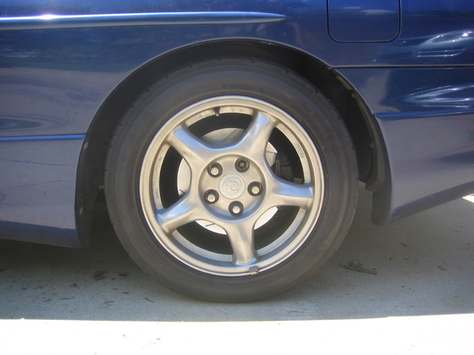 Close-up of a blue car's rear wheel and fender. The wheel has a five-spoke design