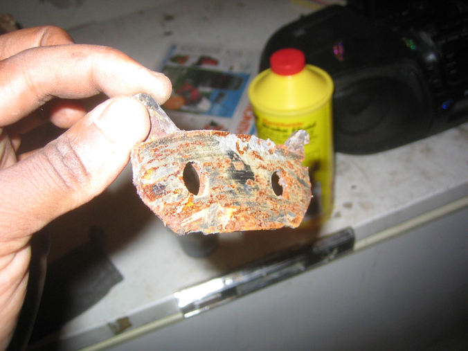 hand holding a rusty metal bracket with two holes