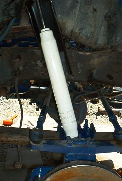 1986 Ford Bronco - Underside view of a vehicle showing a newly installed white shock absorber mounted to blue-painted leaf spring components and a frame rail.…