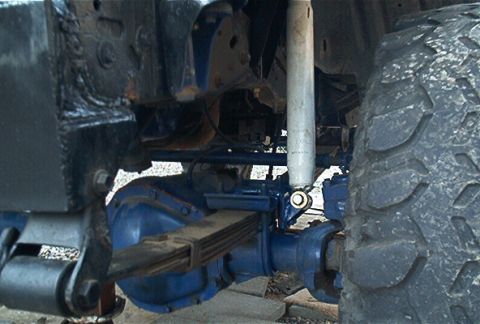 1986 Ford Bronco - Underbody view of a blue-painted front axle and leaf-spring suspension, showing the differential housing, a leaf spring pack, steering link…