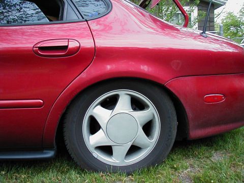 1997 Ford Taurus - Rear quarter panel and wheel of a red 1997 Ford Taurus sedan.