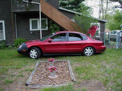 1997 Ford Taurus - A red sedan is parked in front of a house with its trunk open, showing a flower bed in the foreground.