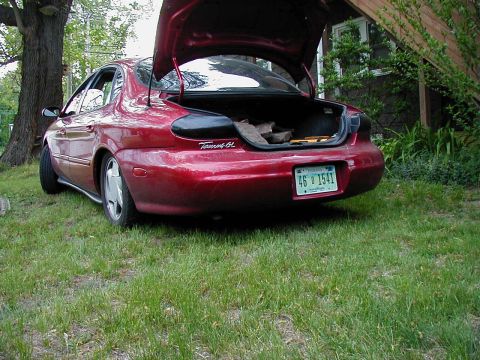 1997 Ford Taurus - Rear view of a red 1997 Ford Taurus GL sedan with its trunk open, parked on a grassy area.