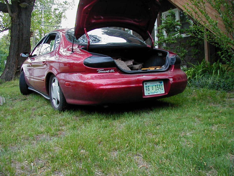 Red 1997 Ford Taurus GL sedan with open trunk, parked on grass