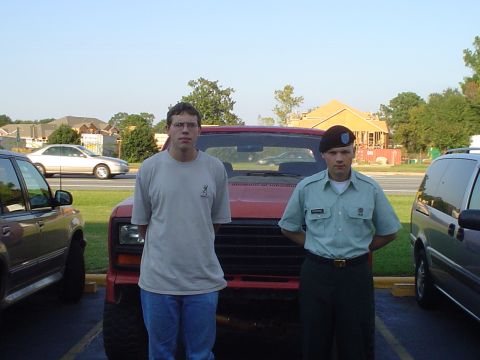 1981 Ford Bronco - Two men pose for a photo in front of a red SUV, with other vehicles in the background.