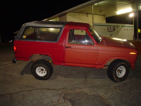 1981 Ford Bronco - A red SUV is parked outside a building at night, showing its side profile.