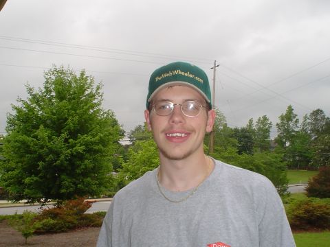 1981 Ford Bronco - Man wearing a green baseball cap and glasses stands outdoors with trees and power lines in the background.