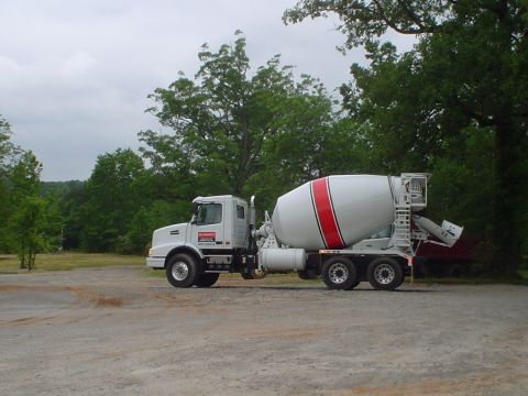 1981 Ford Bronco - A white cement mixer truck is parked on a gravel lot with trees in the background under a cloudy sky.