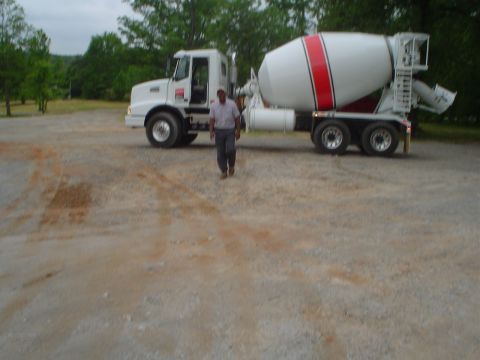 1981 Ford Bronco - A man stands in front of a white cement mixer truck parked on a gravel surface.