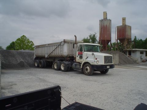 1981 Ford Bronco - A white Volvo dump truck and trailer are parked at a gravel pit with industrial silos in the background.